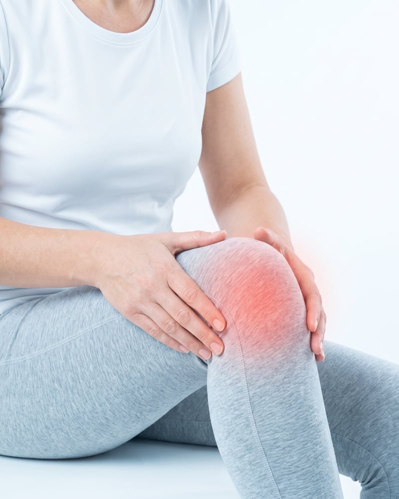 Patientin hält ihr Knie mit rot markiertem Schmerzbereich.