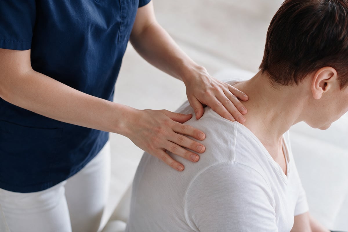 Arzt behandelt die Schulter- und Nackenpartie einer Patientin manuell