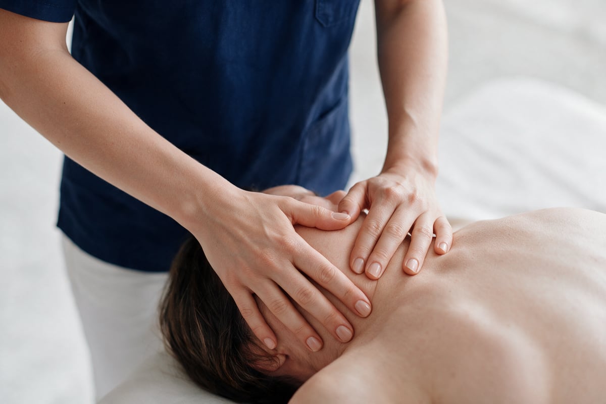 Arzt behandelt die Schulter einer liegenden Patientin osteopathisch