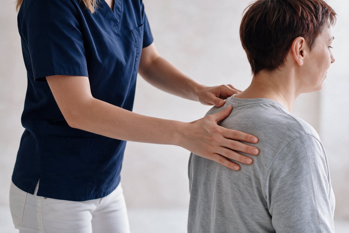Therapeutin untersucht und behandelt die Schulter einer Patientin mit den Händen.